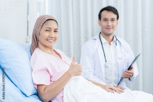 Portrait of Asian woman sick lying down on bed with doctor at hospital. Patient female sitting with man physician feeling happy and smiling together in hospital ward. Health care and insurance concept