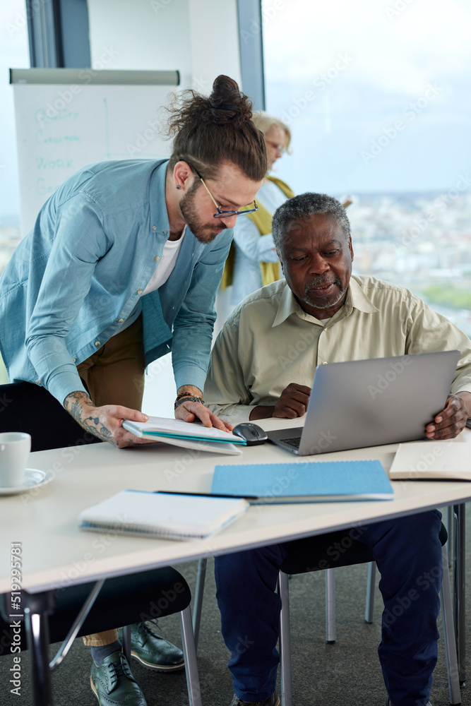 A young teacher explaining to senior student how do computer programming on a laptop.