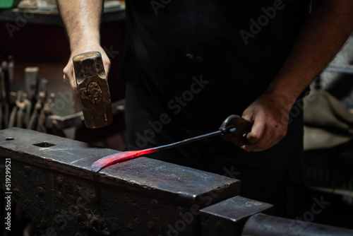 Close up view of heated metal and anvil. Blacksmith in the production process of other metal products handmade in the forge. Metalworker forging metal with a hammer into knife. Metal craft industry.