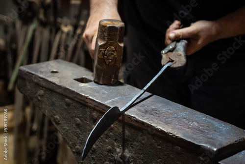 Close up view of heated metal and anvil. Blacksmith in the production process of other metal products handmade in the forge. Metalworker forging metal with a hammer into knife. Metal craft industry. © strigana