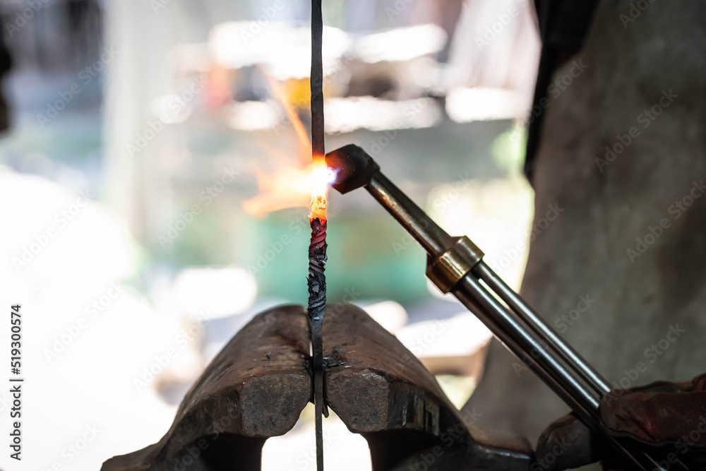 Close up view of heated metal and fire burner. Blacksmith in the production process of other metal products handmade in the forge. Metalworker forging metal into knife. Metal craft industry.