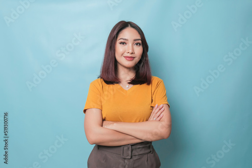Portrait of a confident smiling girl standing with arms folded and looking at camera isolated over blue background