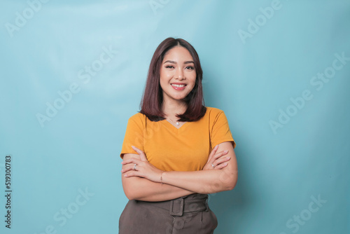 Portrait of a confident smiling girl standing with arms folded and looking at camera isolated over blue background