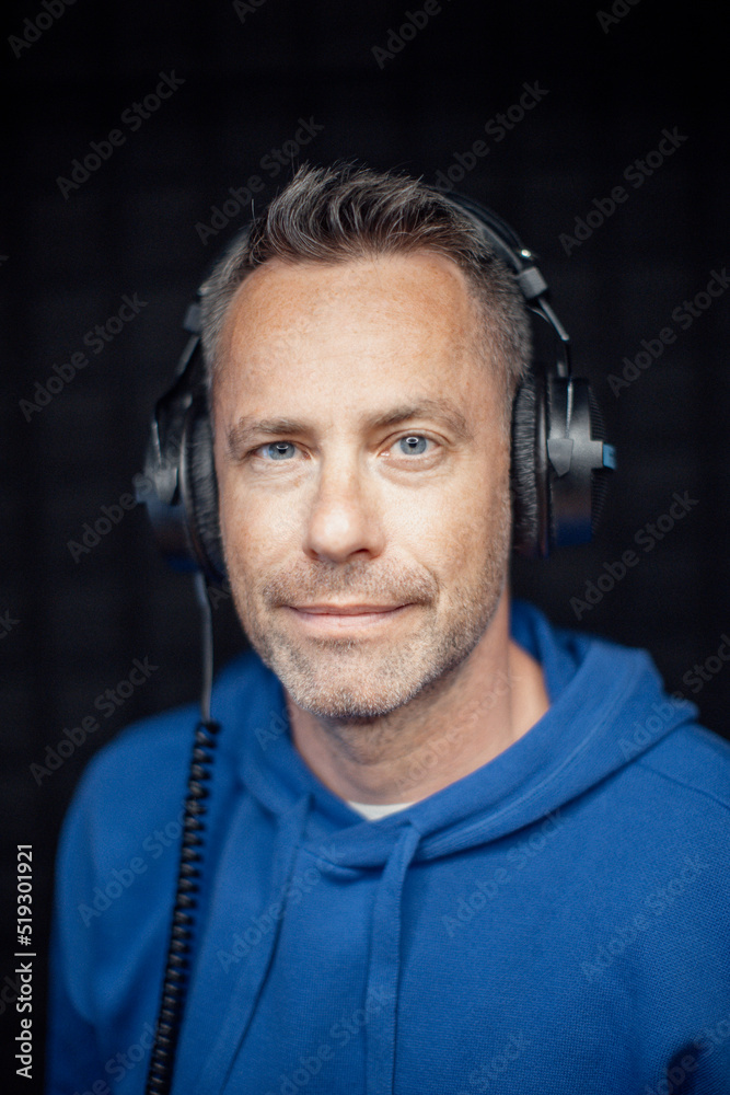 Portrait of male radio host with headphones with arms crossed standing in studio and looking at camera. Portrait of male radio host with headphones with arms crossed standing in studio and looking at camera.