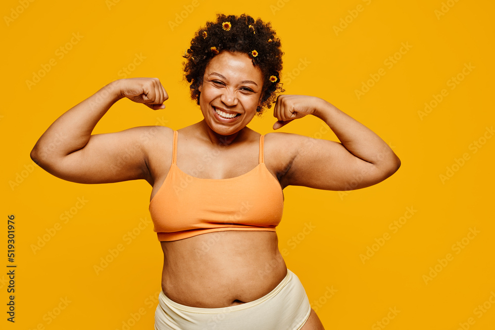 Waist up portrait of powerful black woman smiling happily while posing against vibrant yellow background, body positivity