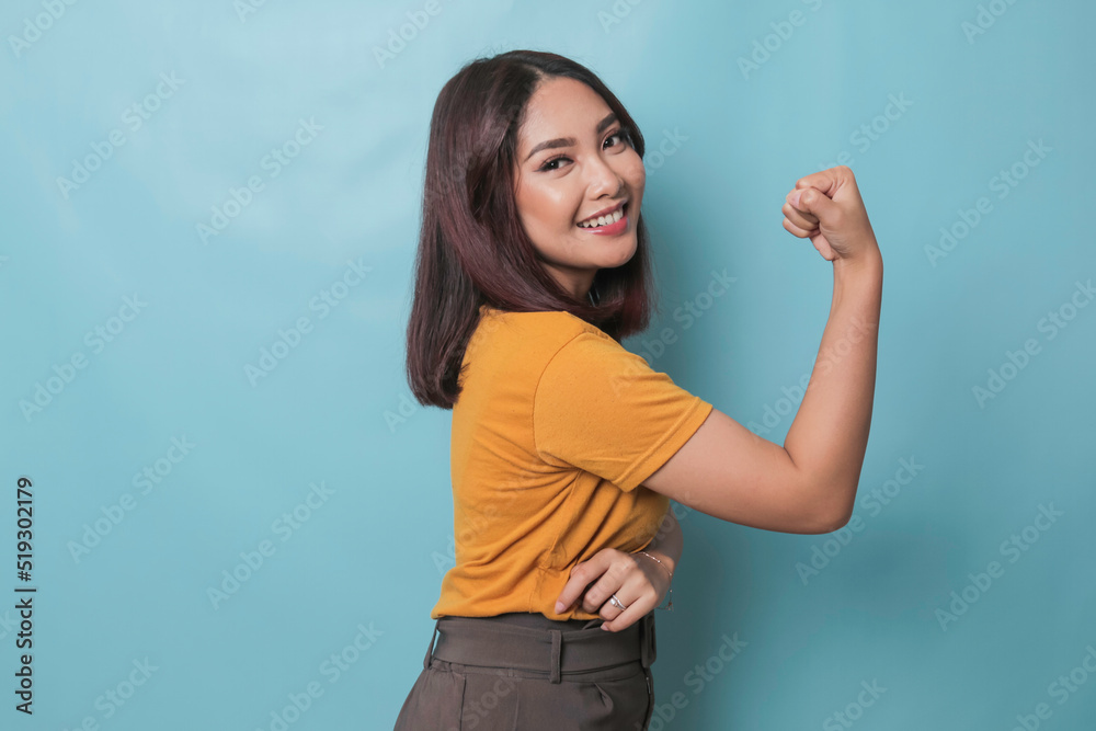 Fototapeta premium Young beautiful girl wearing casual yellow t-shirt standing over isolated blue background showing arms muscles smiling proud. Fitness concept.