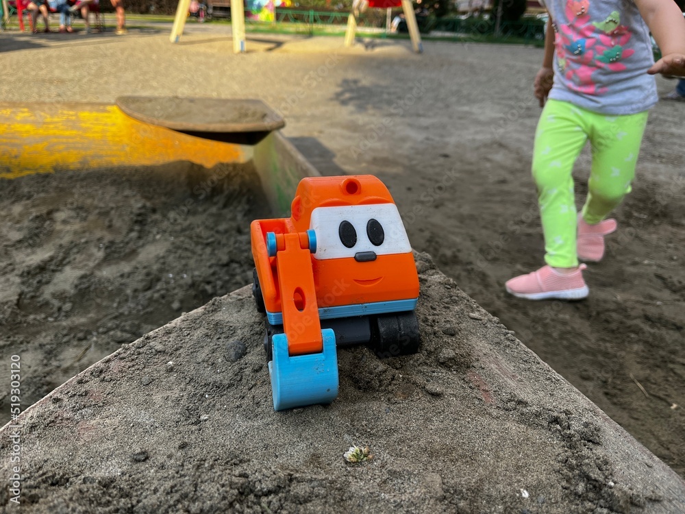 A child slinking to their toy excavator left on the edge of a sandbox on a playground