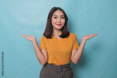 An excited young woman presenting and pointing copy space on her side, isolated on blue background