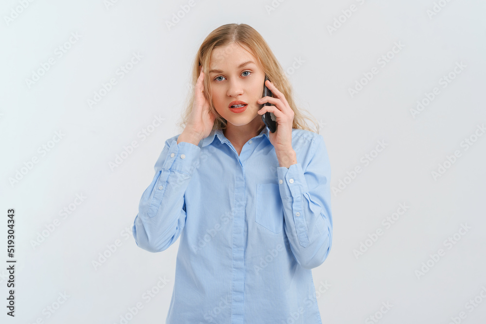 Upset and unhappy blonde woman talking on mobile phone, conversation on smartphone, standing over white background in casual blue shirt. Cellphone, cellular concept Upset and unhappy blonde woman talking on mobile phone, conversation on smartphone, standing over white background in casual blue shirt. Cellphone, cellular concept