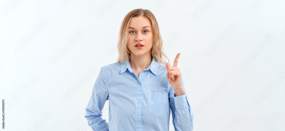 You better not. Serious blonde girl is frowning, pointing fingers up, stands in blue shirt. Indoor studio shot on white background You better not. Serious blonde girl is frowning, pointing fingers up, stands in blue shirt. Indoor studio shot on white background