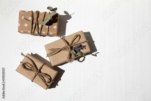 A set of handmade gifts in kraft paper, tied with wide twine, decorated with dry flowers on a white table. Top view