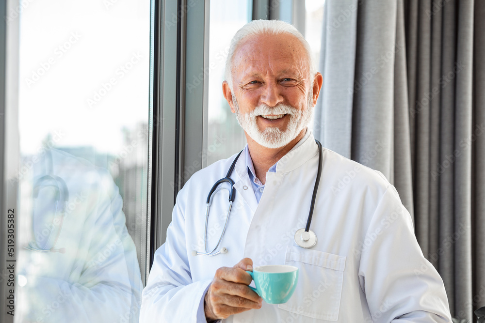 Portrait of senior mature health care professional, doctor, with stethoscope holding blue cup of coffee,