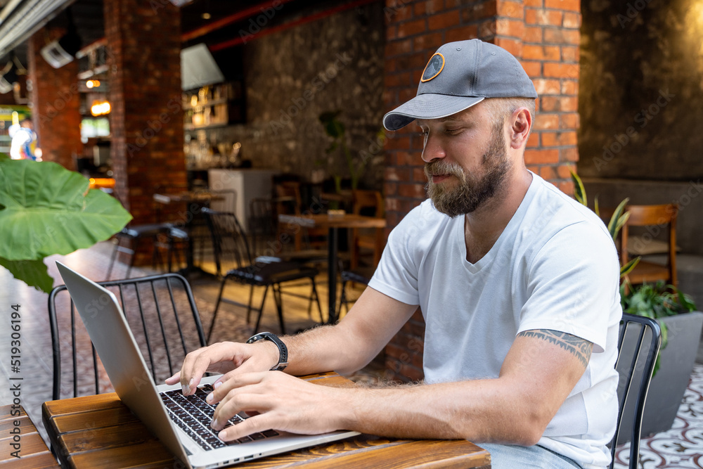 Man in casual clothes working on laptop in cafe or coworking. Typing on keyboard. Remote office work. Casual clothes. Concept of freelance and remote work. Startup business. Create ideas.