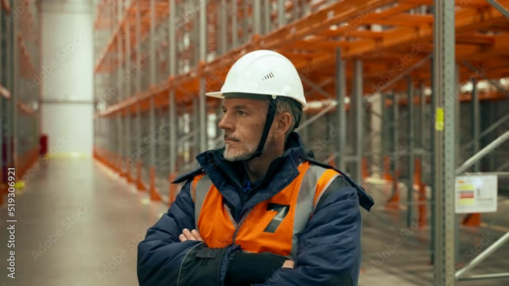 Worried engineer stands with crossed arms on aisle near empty racks in warehouse. Serious bearded man in uniform turns to look in camera closeup Worried engineer stands with crossed arms on aisle near empty racks in warehouse. Serious bearded man in uniform turns to look in camera closeup