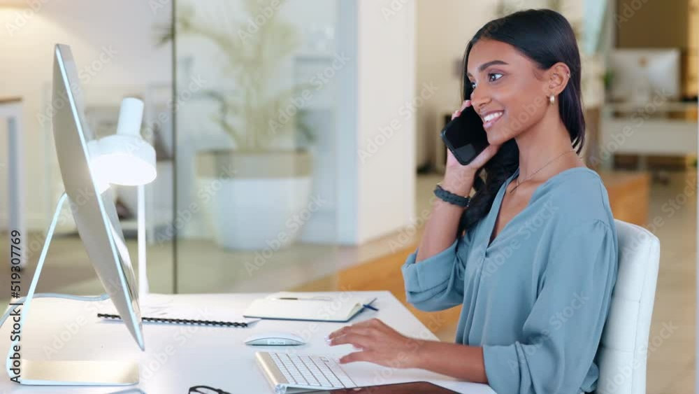 Woman answering a phone call in an office alone at work. One young and happy Indian corporate worker talking, having a conversation and typing a report or replying to emails on a desktop computer Woman answering a phone call in an office alone at work. One young and happy Indian corporate worker talking, having a conversation and typing a report or replying to emails on a desktop computer