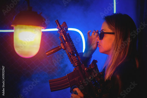 Young futuristic girl with the rifle in the neon lights.