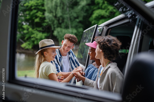 Multiracial young friends travelling together by car, standing by car and smiling - summer vacation, holidays, travel, road trip and people concept.
