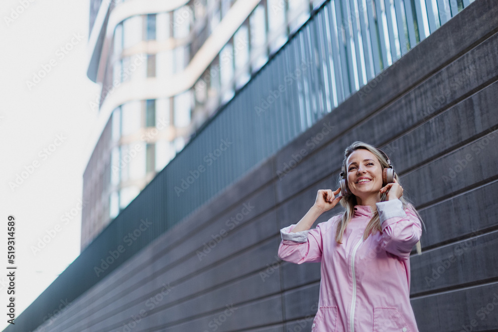 Young woman in city with headphones listening music. Low angle view.
