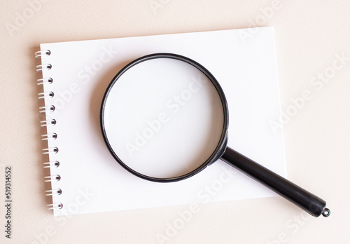 The magnifying glass lies on the notebook on a white page.