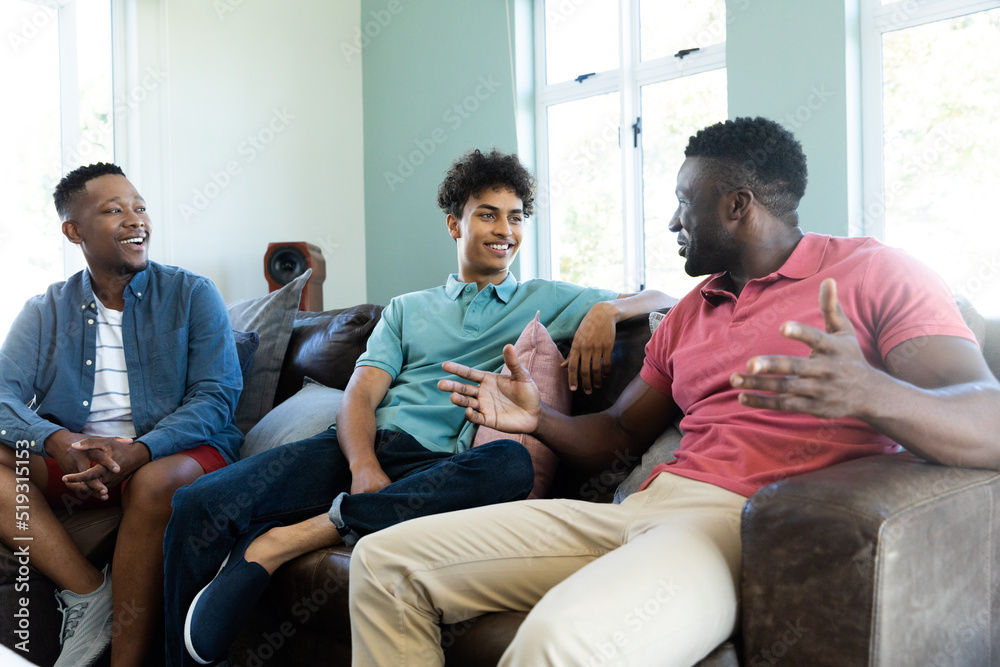 Multiracial young male friends talking while relaxing on armchairs in living room, copy space Multiracial young male friends talking while relaxing on armchairs in living room, copy space