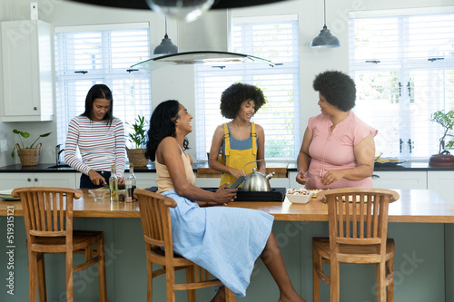 Biracial female friends talking and cooking food at kitchen island while enjoying weekend at home