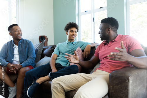 Multiracial young male friends talking while relaxing on armchairs in living room, copy space
