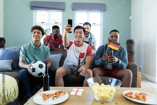 Multiracial male friends with beer bottles, flags and ball watching soccer match at home, copy space