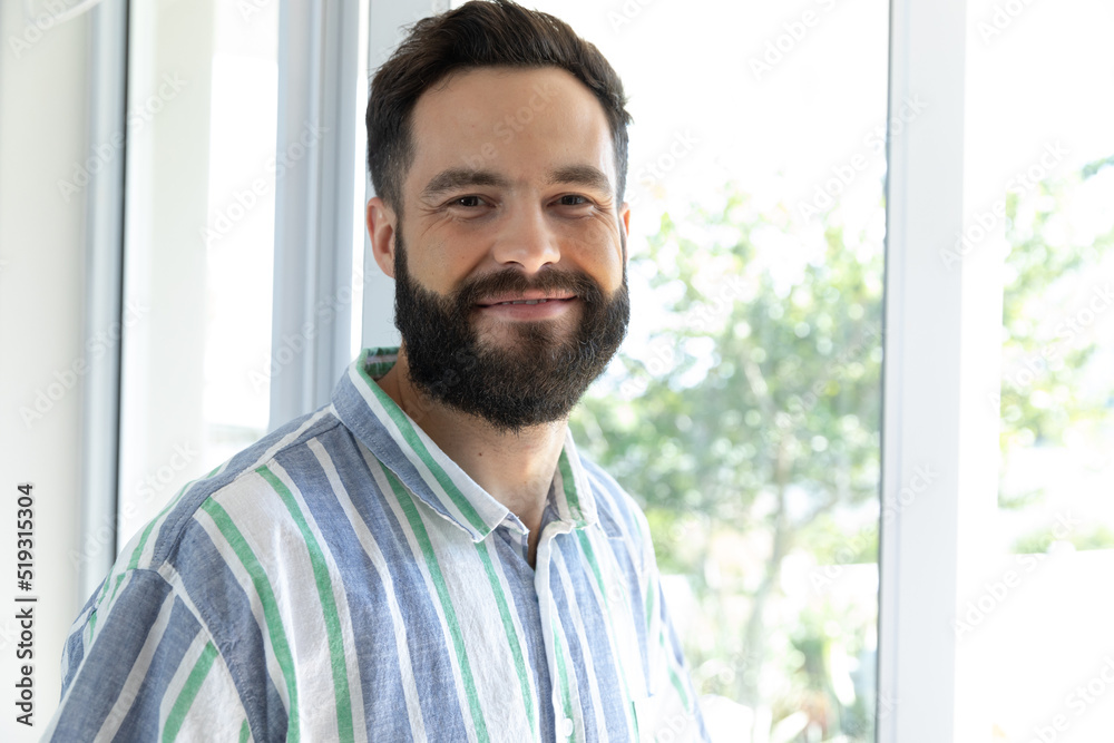 Portrait of smiling caucasian young man with beard and mustache by window at home, copy space Portrait of smiling caucasian young man with beard and mustache by window at home, copy space