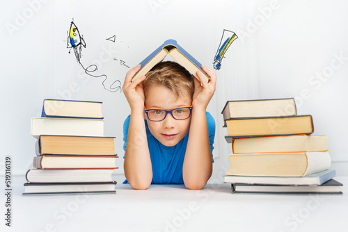 smiling boy with many books holds the book as a roof over his head. Safety in learning concept.