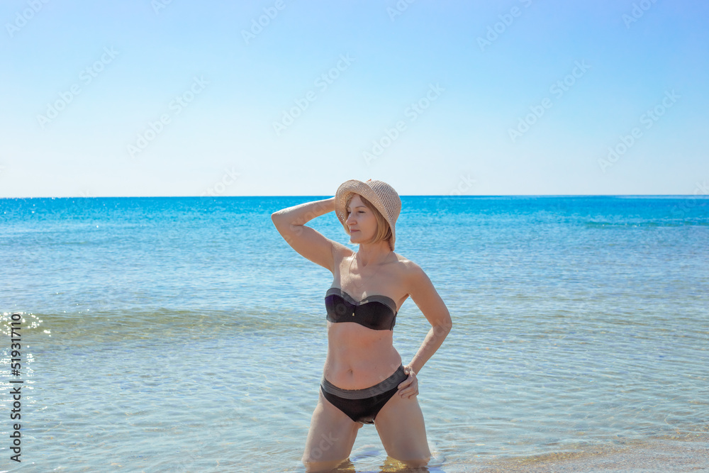 An adult woman in a swimsuit poses on the sea coast in summer. Rest and relaxation.