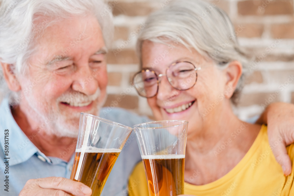 Defocused senior smiling couple toasting with a glass of blonde beer Defocused senior smiling couple toasting with a glass of blonde beer