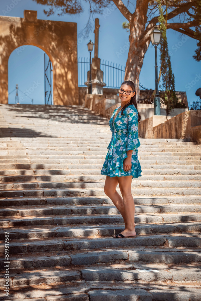 young woman in summer dress and glasses standing on a staircase 