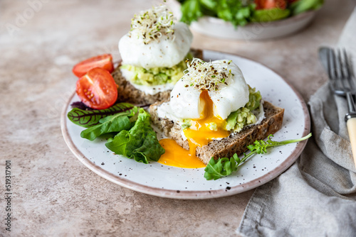 Sourdough bread with cream cheese, mashed avocado and poached egg served with salad, tomatoes and sprouts on concrete background. Healthy breakfast or brunch. Diet food concept.