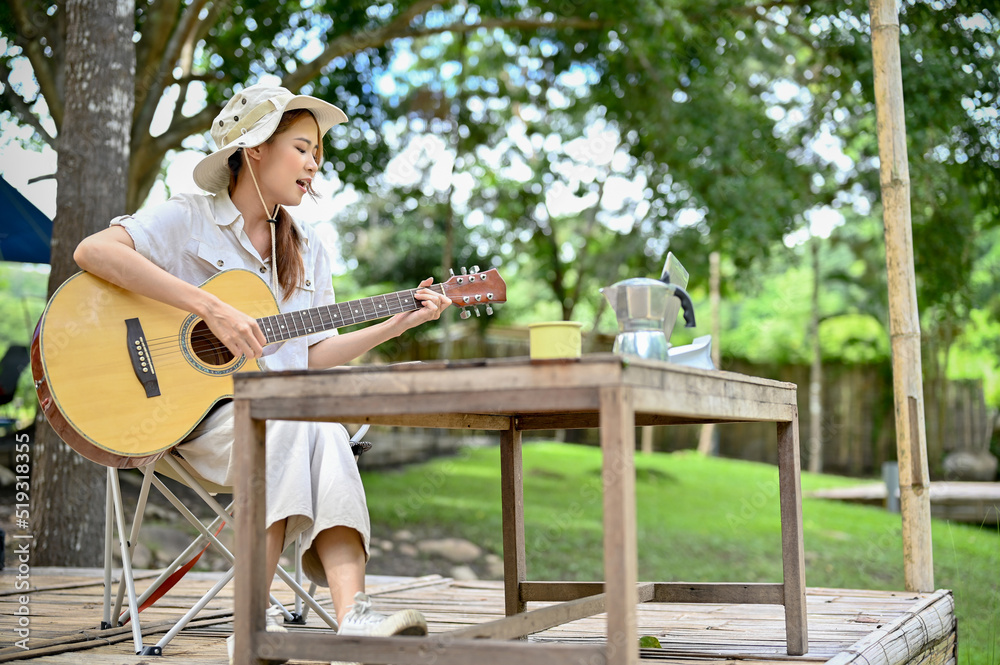 Attractive and relaxed young Asian female camper singing her song and playing guitar