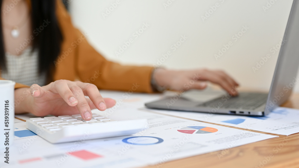 Cropped, Female accountant working at her office desk, using calculator and laptop. Cropped, Female accountant working at her office desk, using calculator and laptop.