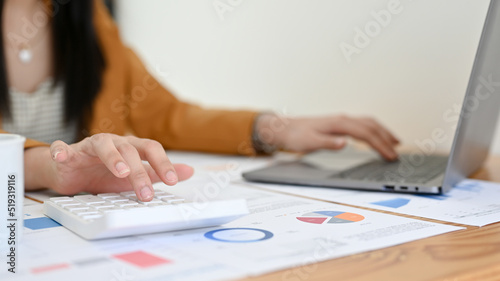 Cropped, Female accountant working at her office desk, using calculator and laptop.