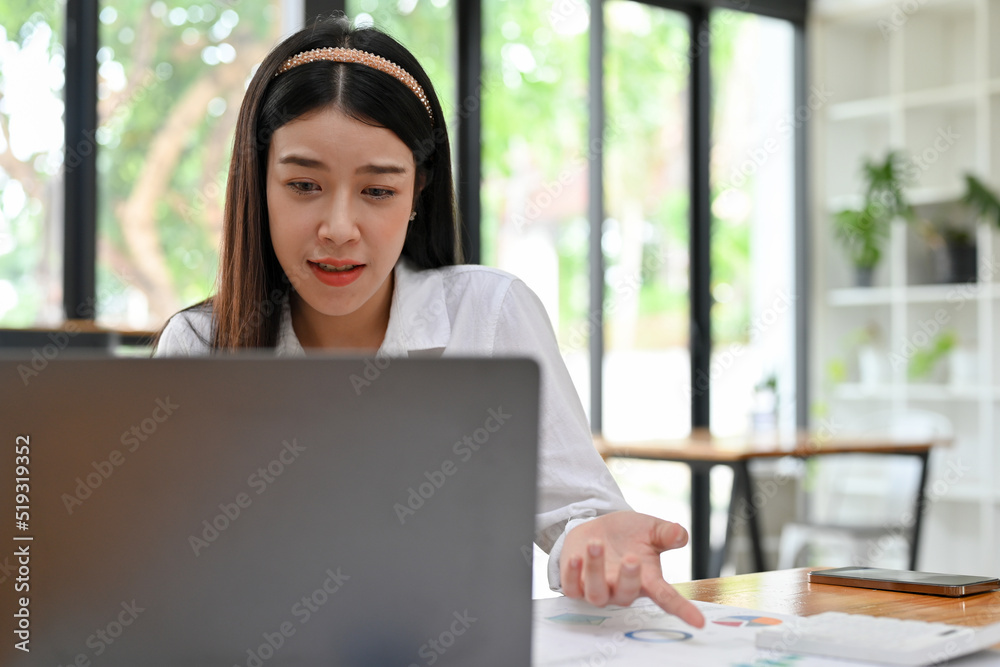 Beautiful Asian businesswoman is working on her project, using laptop computer.