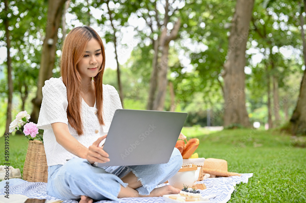 Attractive young Asian female picnicking in the park and using portable laptop. Attractive young Asian female picnicking in the park and using portable laptop.