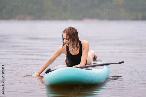 A beautiful girl is floating on a supboard on a river. Young woman supsurfing at sunrise. © deine_liebe