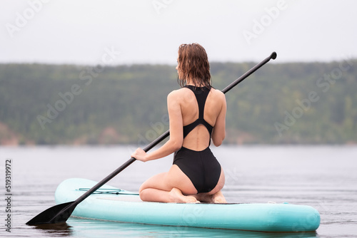 A beautiful girl is floating on a supboard on a river. Young woman supsurfing at sunrise.
