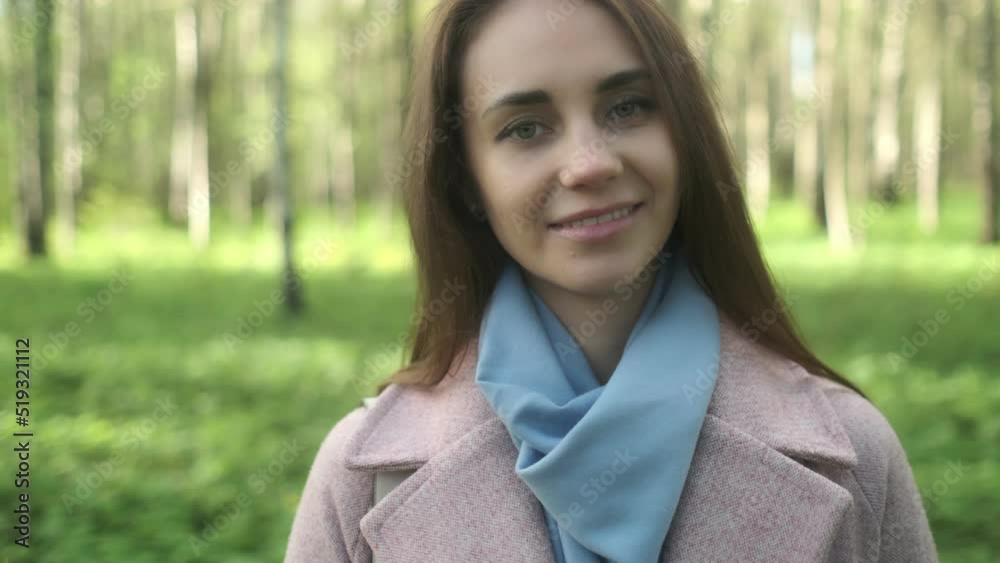 Close-up portrait of smiling woman standing in park garden outdoors. A flirtatious cute pretty girl with long hair is looking at the camera and smiling. Close-up portrait of smiling woman standing in park garden outdoors. A flirtatious cute pretty girl with long hair is looking at the camera and smiling.