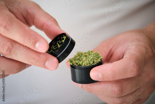 Two hands holding marijuana grinder with milled cannabis female flower. Herb grinder. photo