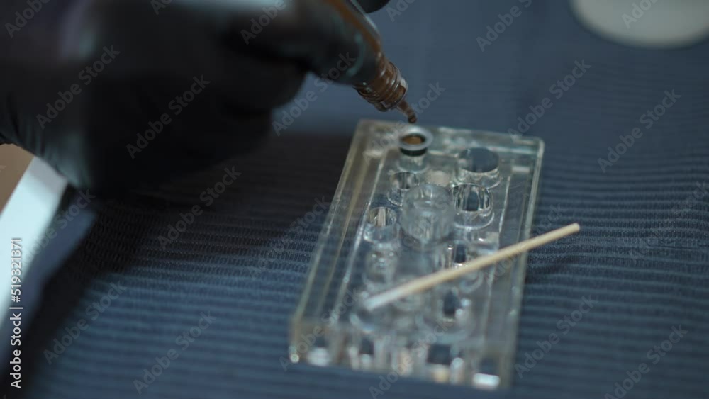 Close-up adding brown pigment to black ink in ring cup in beauty salon. Unrecognizable beautician tattoo master in gloves preparing color for permanent makeup tattooing indoors