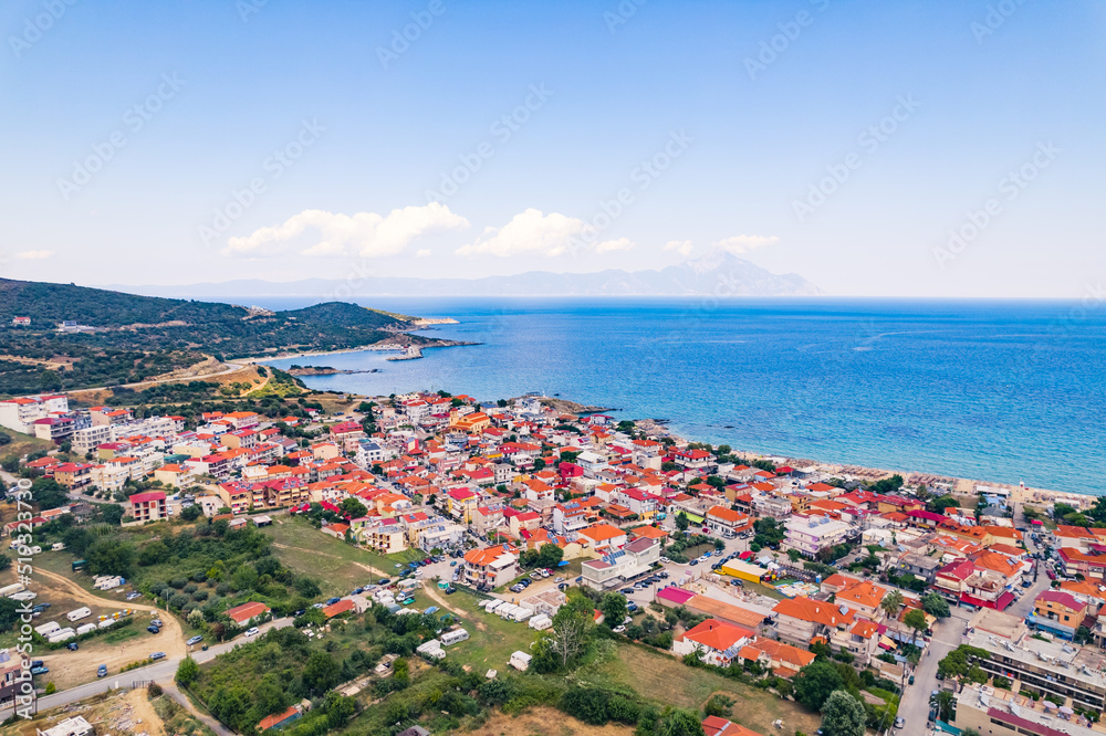 Aerial drone view of Greek seashore filled with whitewashed houses with vivid orange tiles. Nearly cloudless weather, sunshine, and blue sky. High quality photo