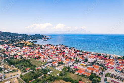 Aerial drone view of Greek seashore filled with whitewashed houses with vivid orange tiles. Nearly cloudless weather, sunshine, and blue sky. High quality photo