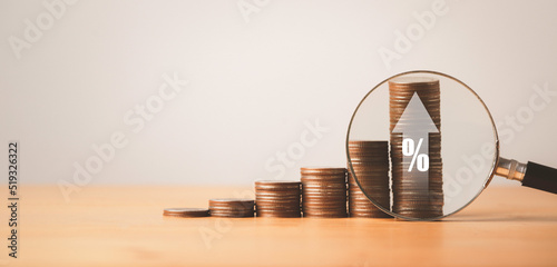 Magnifier glass with increasing coins stacking with up arrow and percentage sign for interest debt and financial banking deposit concept.