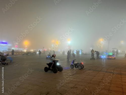  Crowd  of people walking in a public square on a foggy night photo