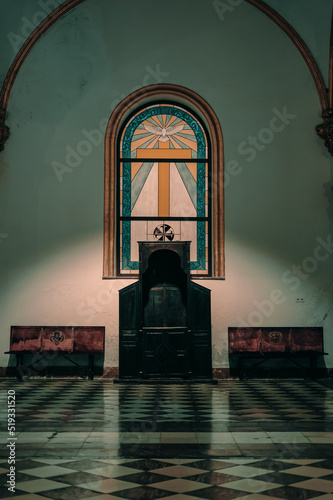 Confessional of a church with pews on the sides and a stained glass window in the background