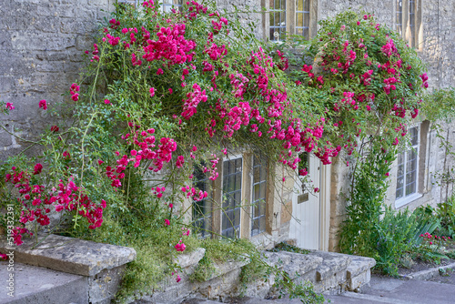 Fototapeta Naklejka Na Ścianę i Meble -  Pink roses groiwng over thewall of a traditional stone cottage in the Cotswolds