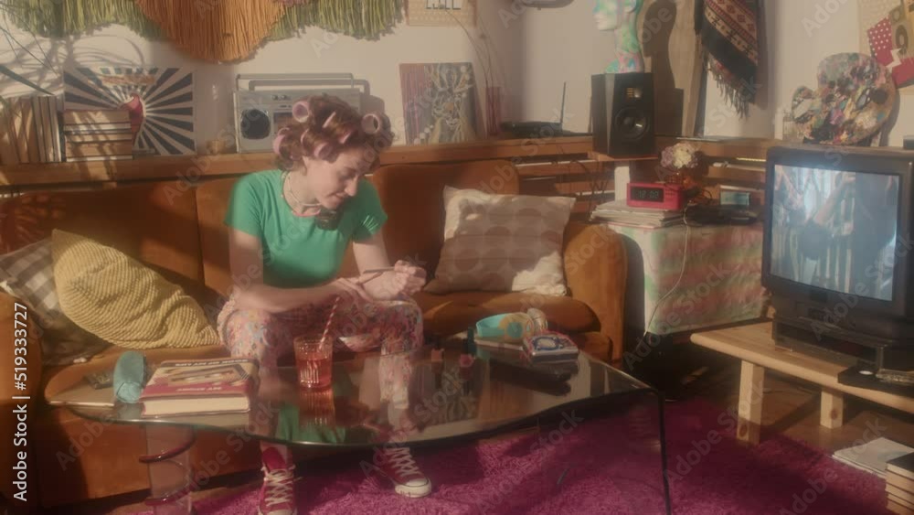 Tracking in of young girl in curlers doing her manicure, talking on phone, watching TV at home in eighties Tracking in of young girl in curlers doing her manicure, talking on phone, watching TV at home in eighties